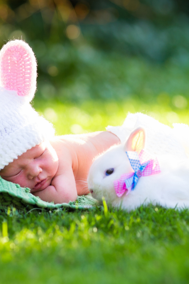 Маленький спящий грудной ребенок на зеленой траве с белым кроликом