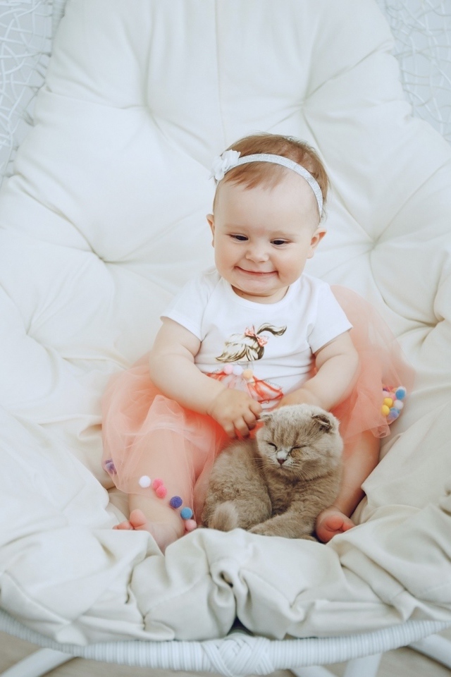 Маленький улыбающийся ребенок с котом сидит в белом кресле
