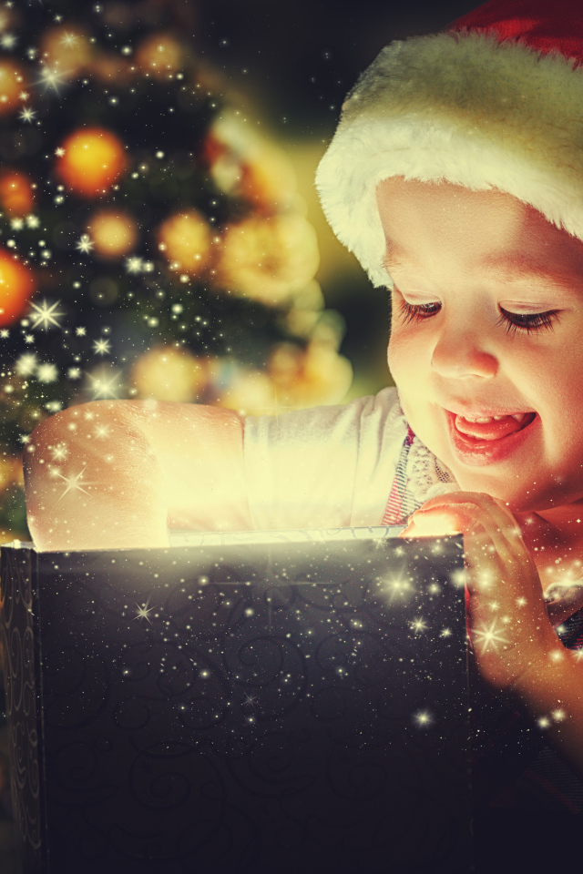 Маленькая улыбающаяся девочка открывает подарок у новогодней елки 