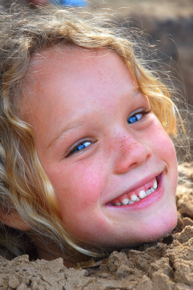 Маленькая улыбающаяся девочка играет в песке