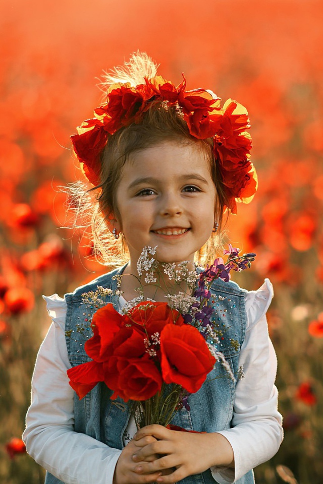 Маленькая улыбающаяся девочка с венком из красных маков на голове и букетом в руках