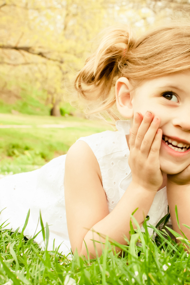 Улыбающаяся девочка в белом платье лежит на зеленой траве