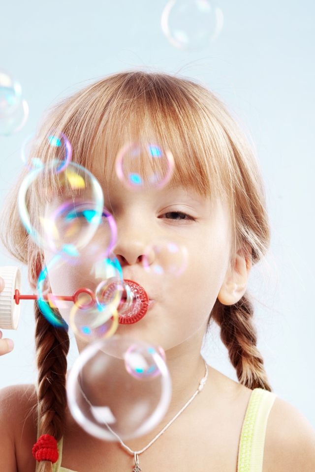 Девочка с косичками пускает мыльные пузыри