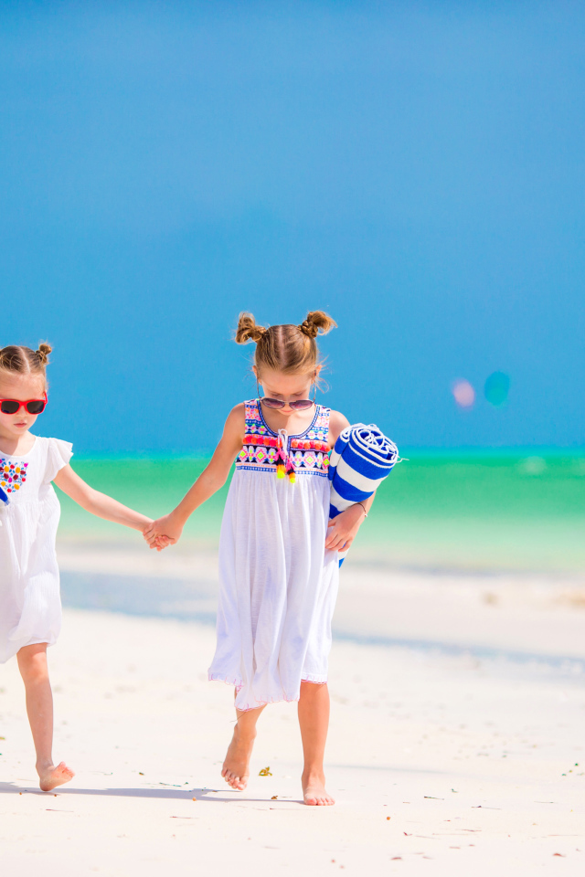 Две маленькие девочки идут по песку