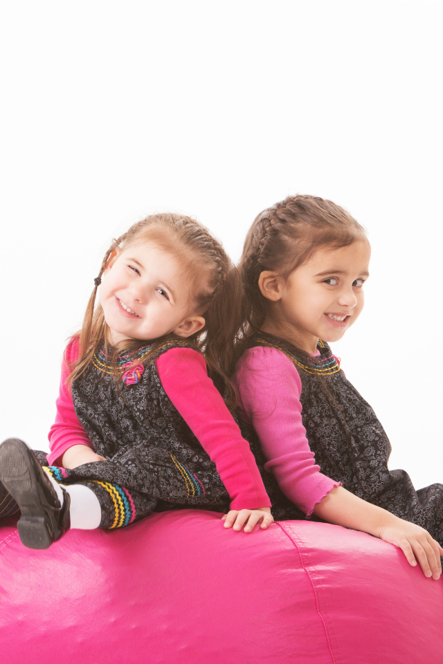 Две маленькие девочки сидят на красном мягком шаре 