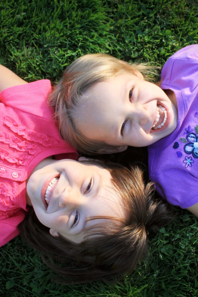 Две маленьких улыбающихся девочки лежат на зеленой траве