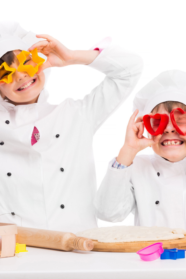Два маленьких ребенка в костюмах повара готовят на кухне печенье