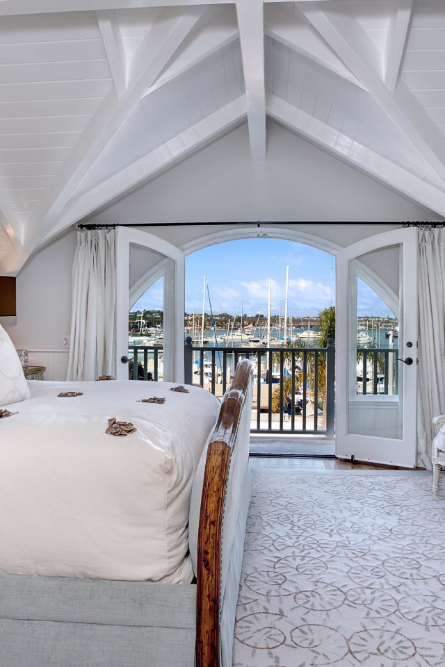 Белая спальня с большой высокой кроватью и балконом 