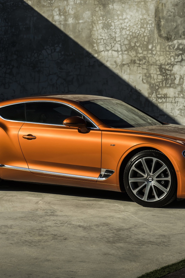 Оранжевый автомобиль Bentley Continental GT V8, 2019 года на фоне стены