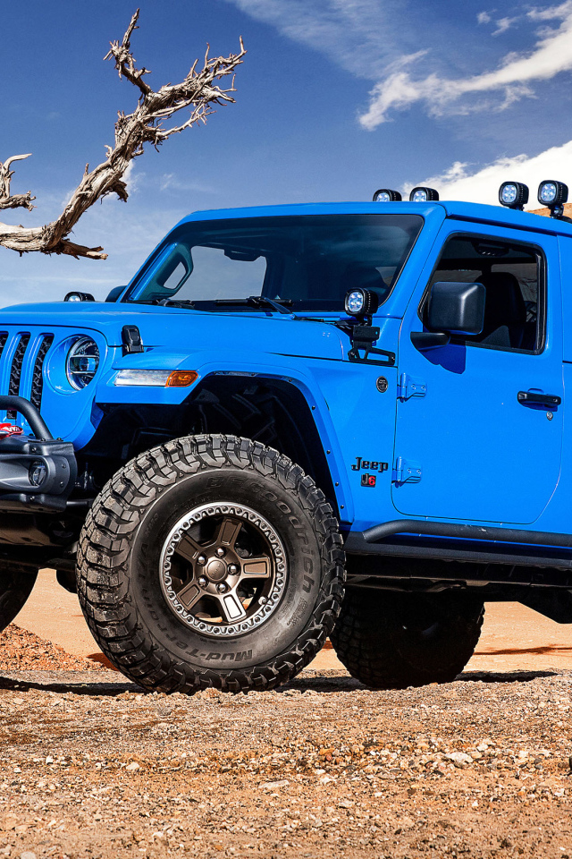 Синий пикап Jeep J6, 2019 года на фоне гор у сухого дерева