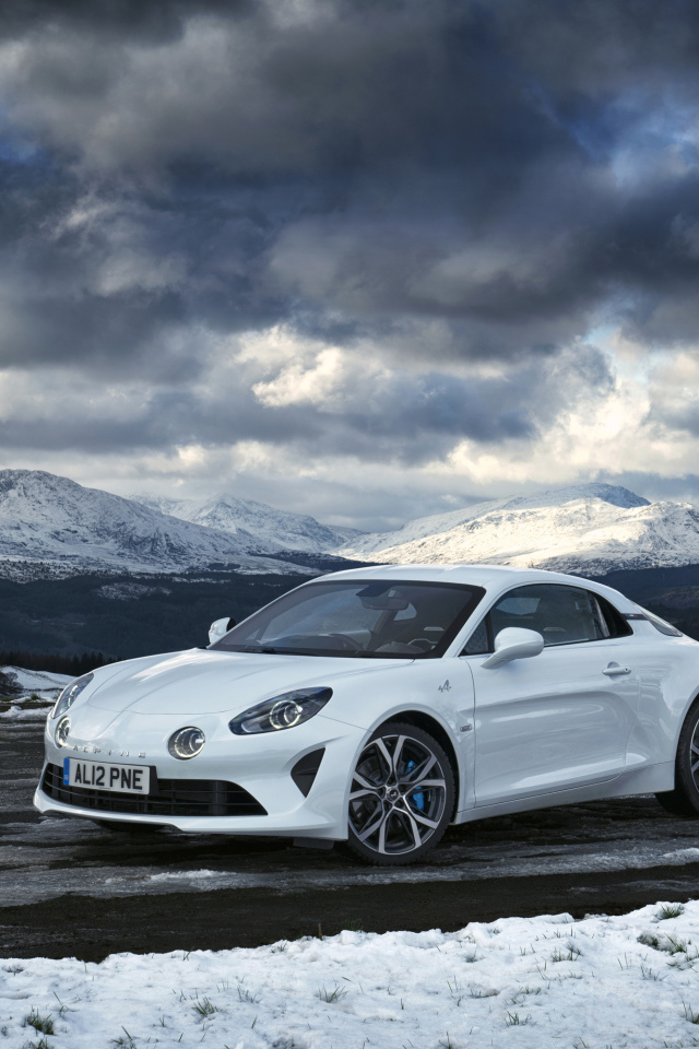Белый автомобиль Alpine A110 на фоне гор под грозовым небом  