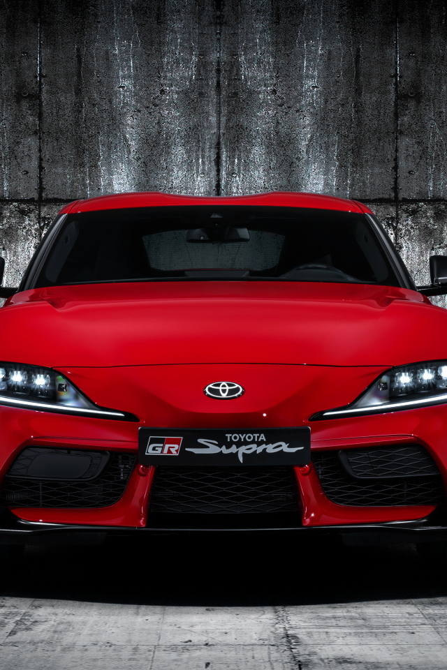 Красный автомобиль Toyota GR Supra 2019 года на фоне серой стены