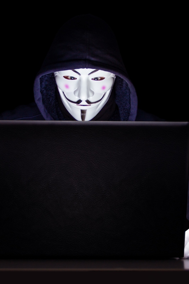 Хакер анонимус в маске и худи за ноутбуком