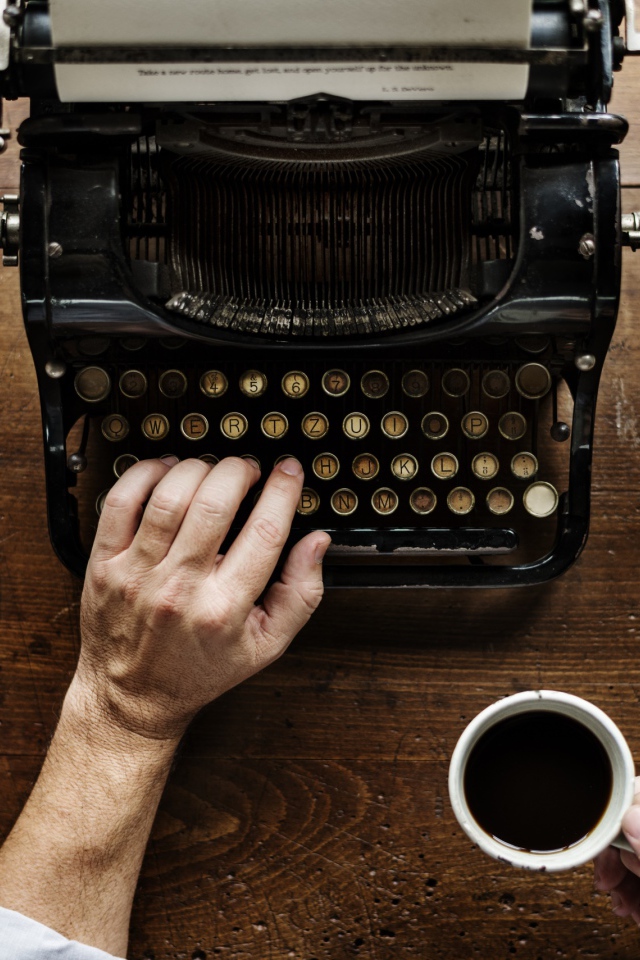 Мужчина с чашкой кофе в руке печатает на старой печатной машинке 