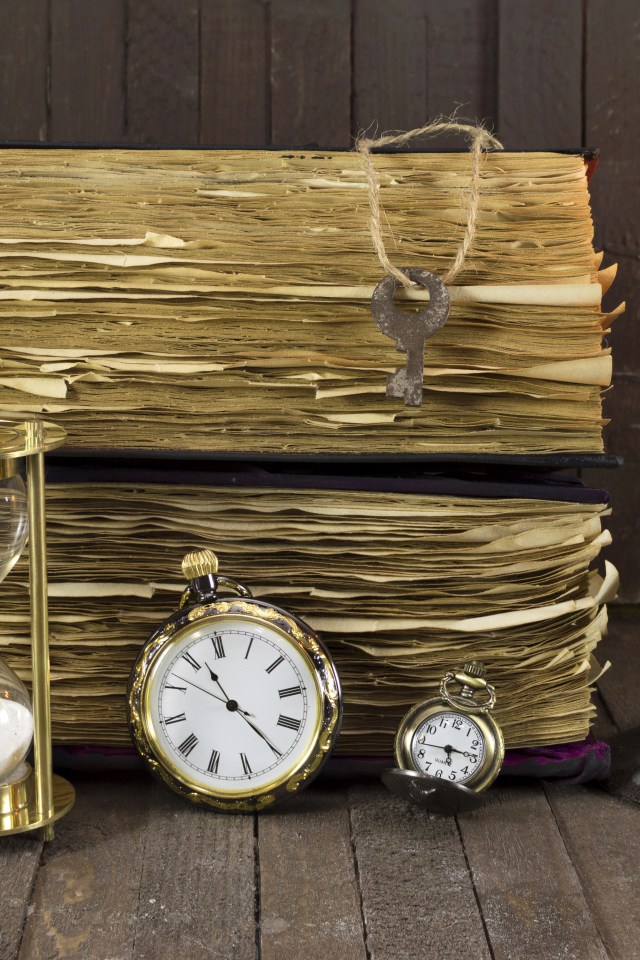 Старинные книги, зажженная свеча, ключи и часы на столе