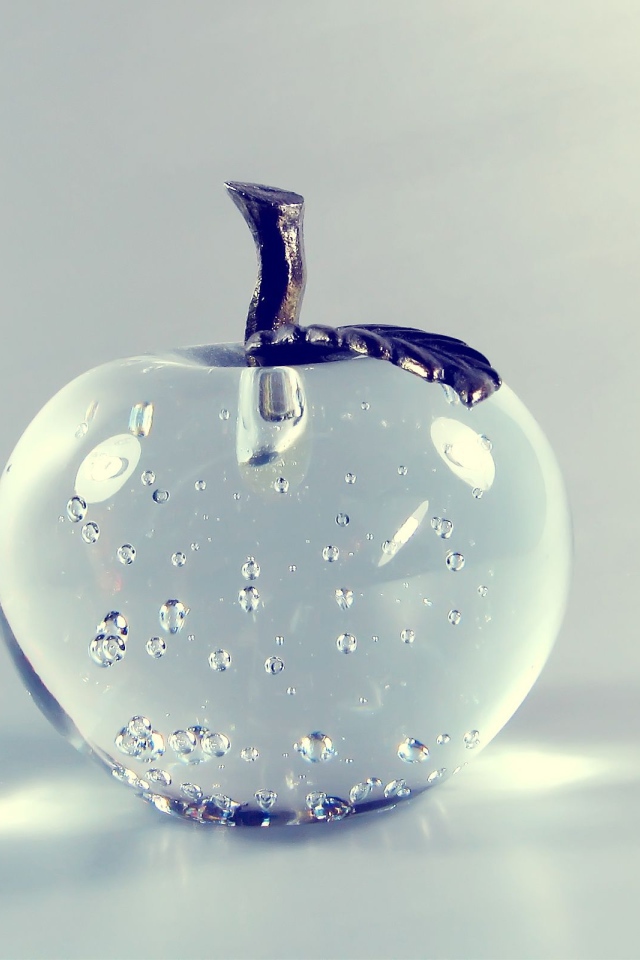 Стеклянное яблоко на сером фоне 