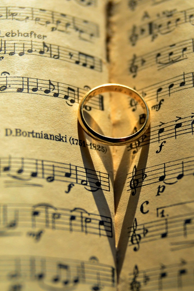 Золотое обручальное кольцо лежит на нотной тетради