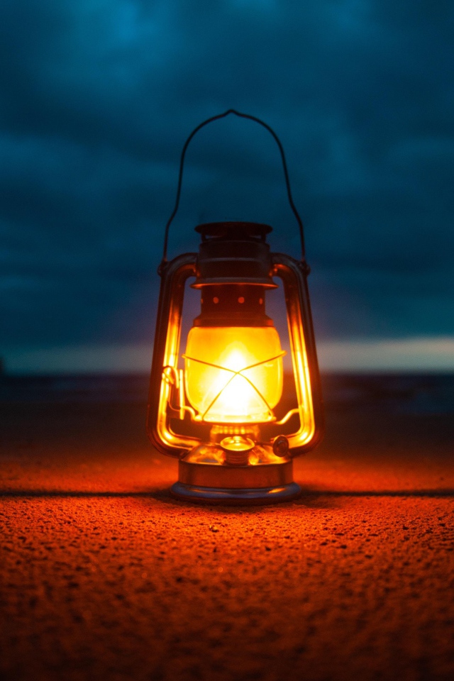 Включенный фонарь стоит на песке у моря 