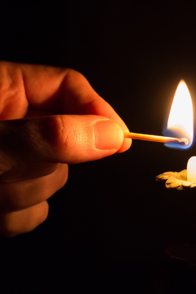Рука со спичкой поджигает свечу