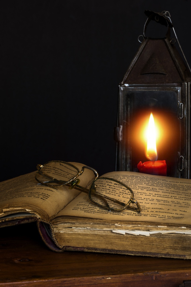 Старая книга с очками на столе со свечой 