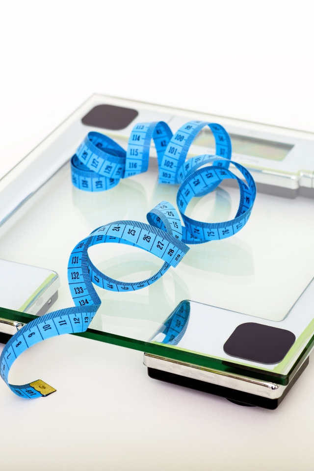 Весы на полу с сантиметром на белом фоне