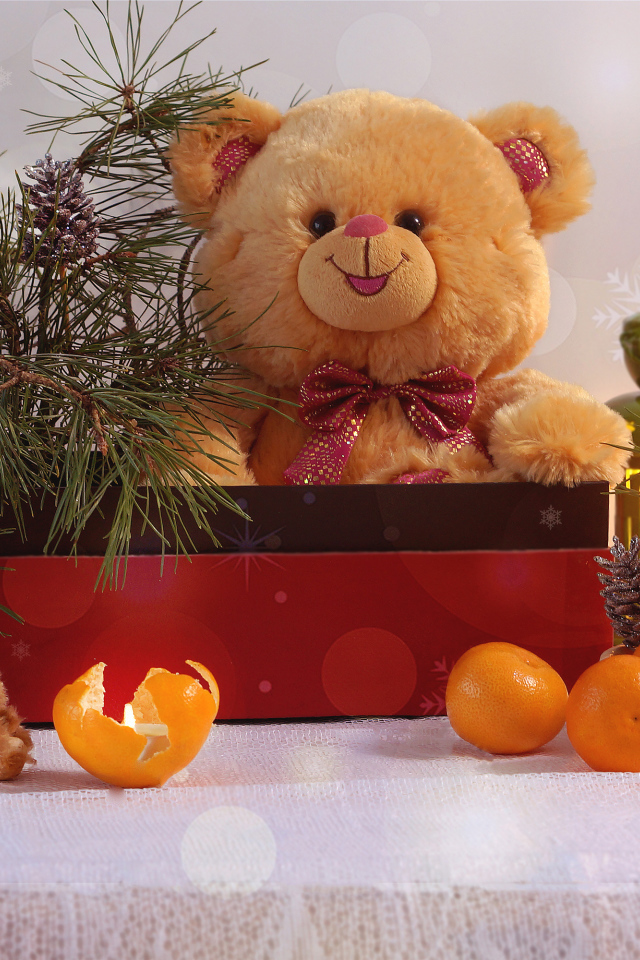 Медвежонок Тедди в коробке с еловой веткой на столе с мандаринами 