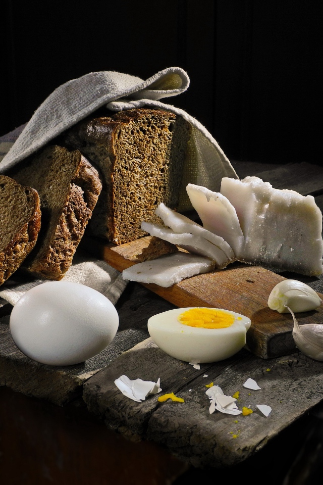 Черный хлеб, вареные яйца, чеснок и сало на деревянном столе