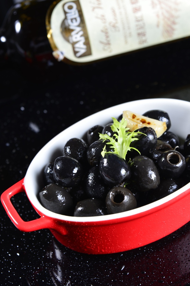 Черные оливки на столе с бутылкой и помидорами