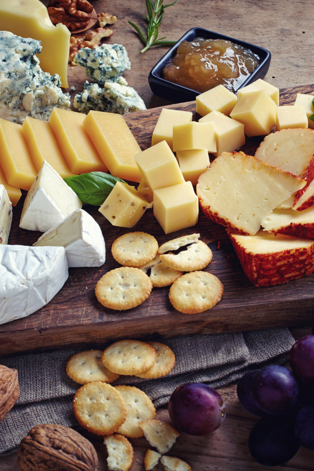 Сырная нарезка на разделочной доске на столе с виноградом и крекерами