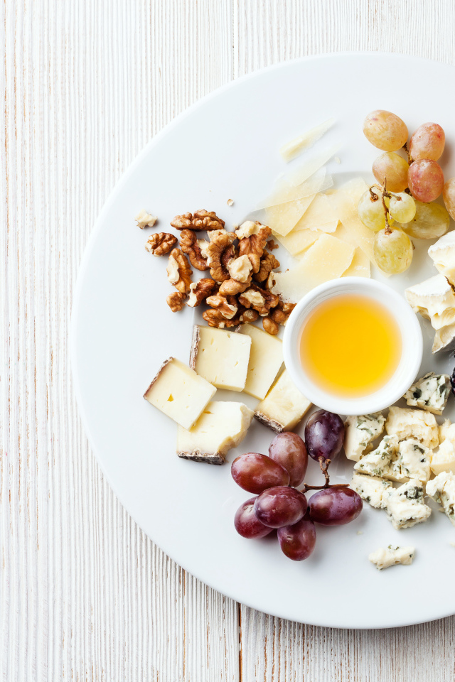 Куски сыра на тарелке с орехами, виноградом, медом и ягодами ежевики