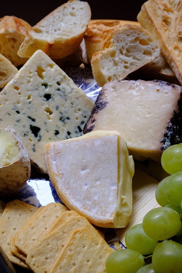 Разные виды твердого сыра на тарелке с белыми виноградом и вином