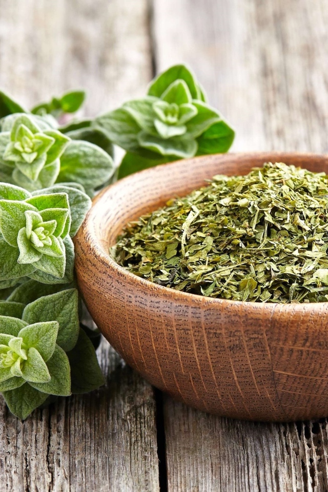 Сухая трава орегано в деревянной миске на столе 