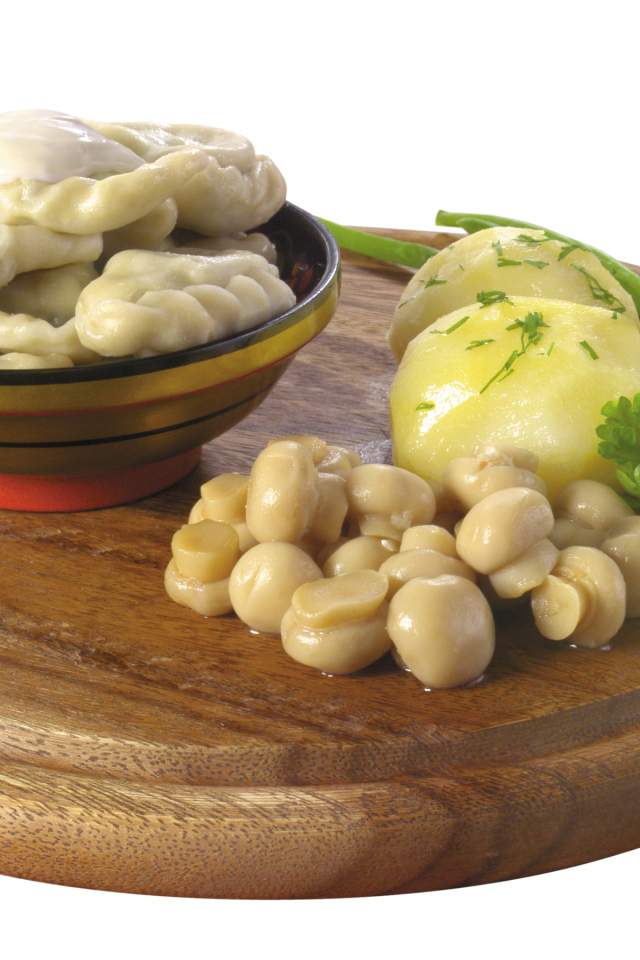 Вареники с грибами и вареной картошкой на деревянной доске на белом фоне