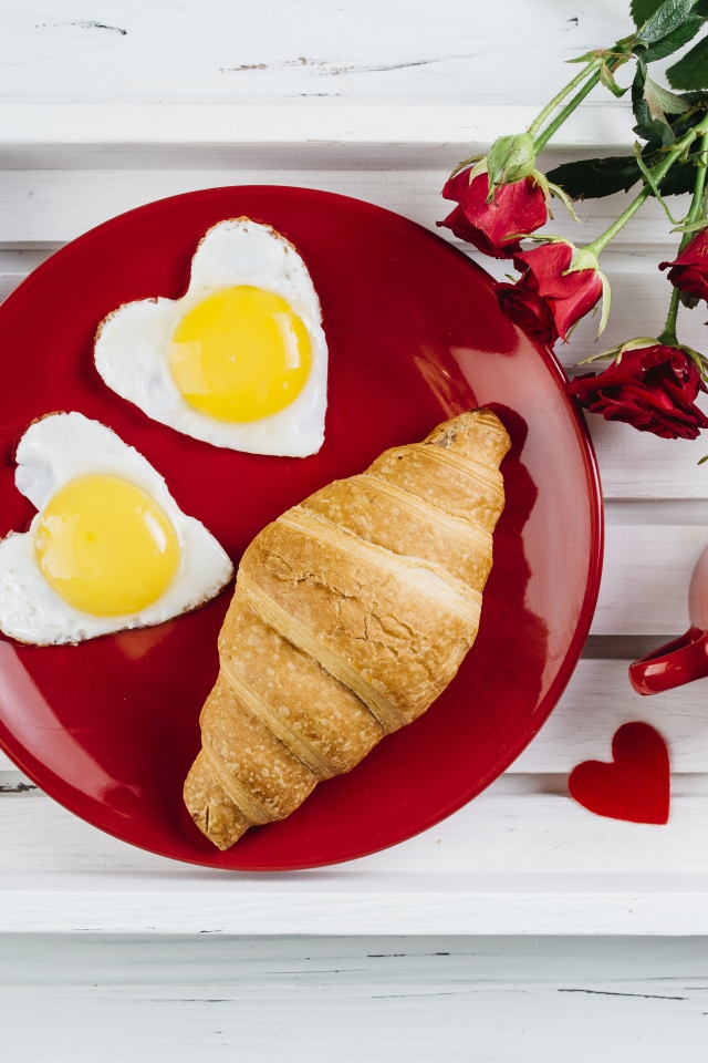Яичница с круассаном на красной тарелке на столе букетом роз и чашкой какао