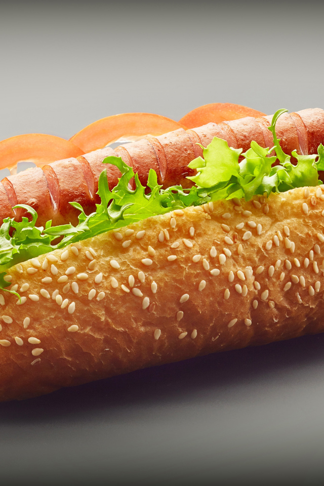 Хотдог с сосиской гриль и листьями салата на сером фоне