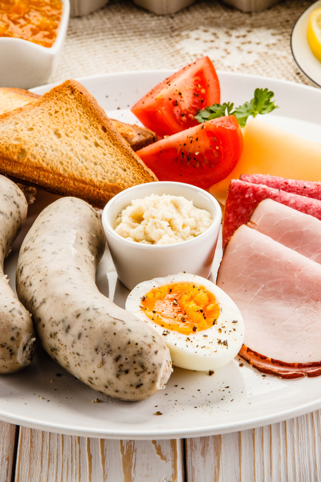 Большая белая тарелка с колбасой, яйцами, помидорами, тостами и сыром