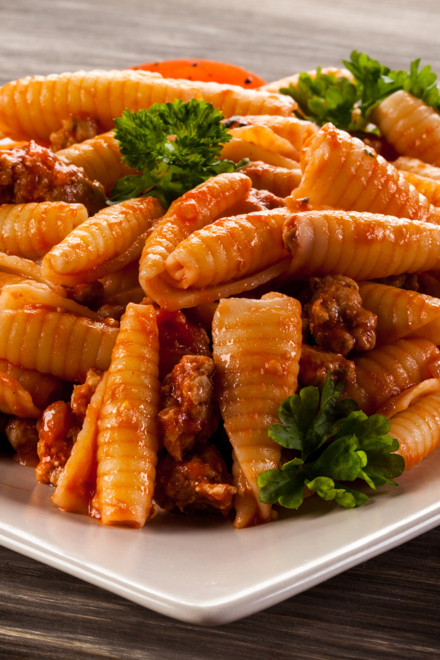 Паста с мясом, петрушкой и помидорами на белой тарелке