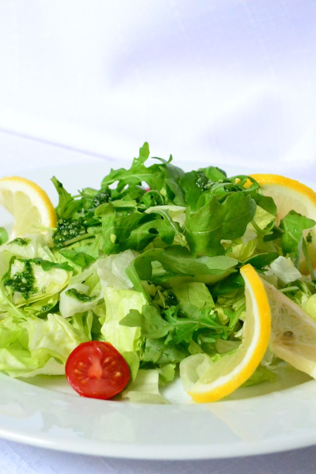 Салат с рукколой, лимоном и помидорами на белой тарелке