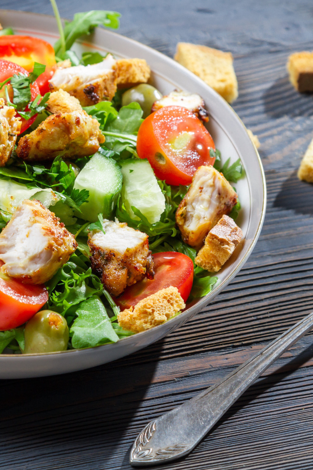 Салат с овощами, сухариками и курицей и на столе с вилкой