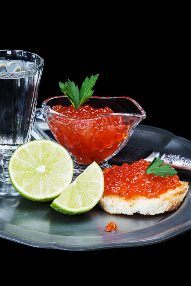 Бутерброды с красной икрой на подносе с рюмкой водки и лаймом
