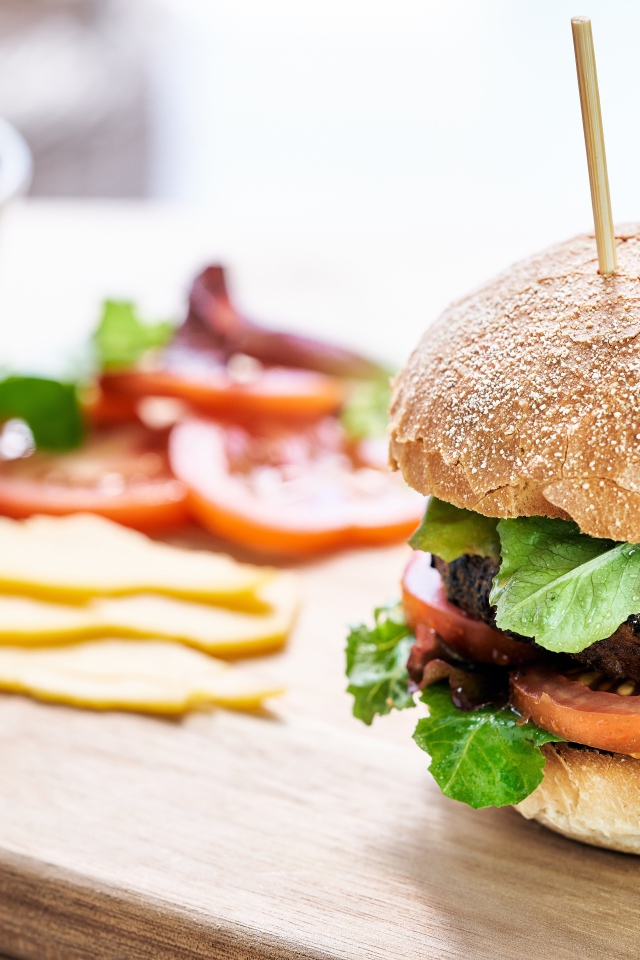 Аппетитный гамбургер на доске с сыром и помидорами