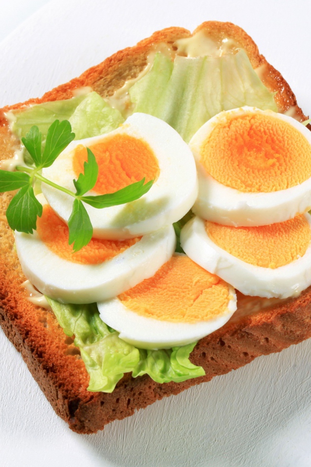 Тост с листом салата и кусочками яйца на белой тарелке 