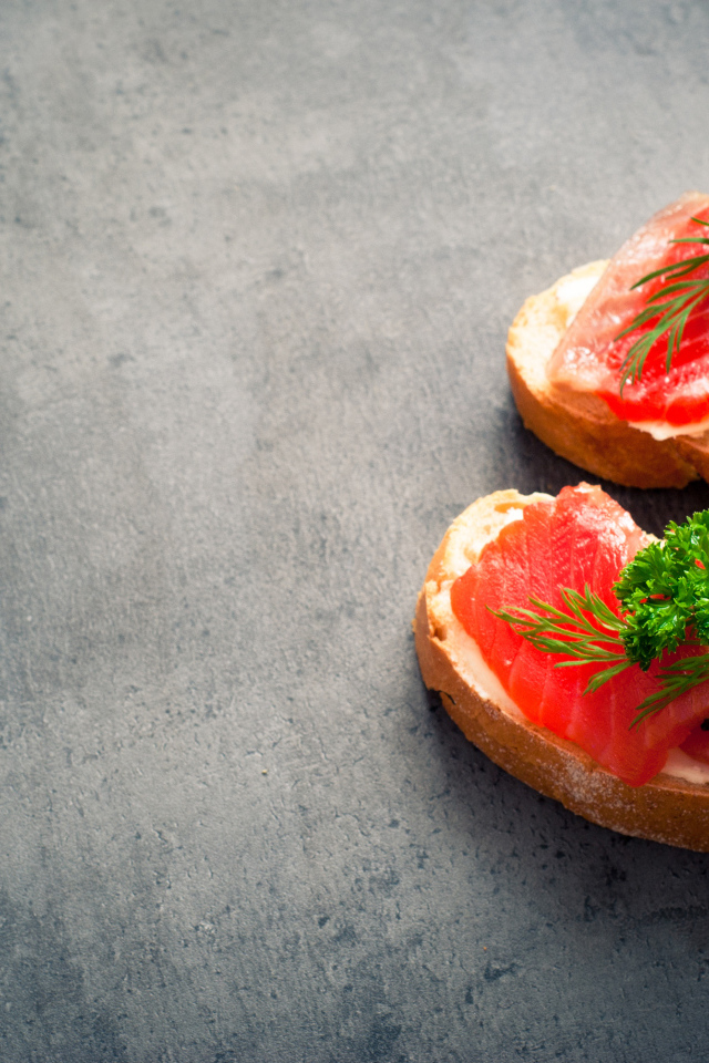 Два бутерброда с красной рыбой, огурцом и зеленью на черном фоне