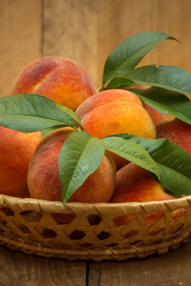 Корзинка персиков с зелеными листьями на столе