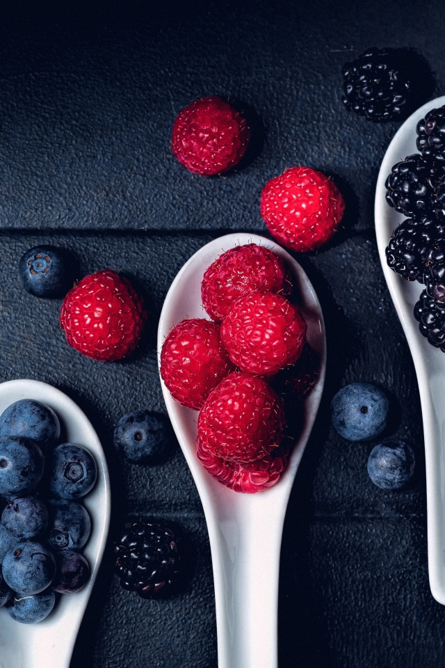 Ягоды черники, малины и ежевики на белых ложках