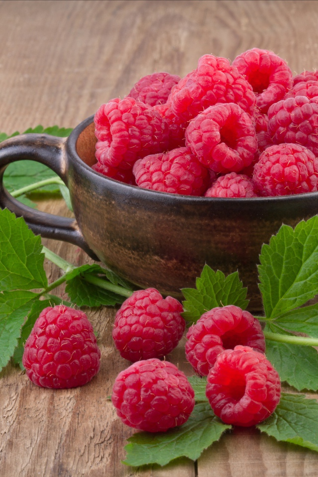 Чашка со свежей малиной на столе с зелеными листьями