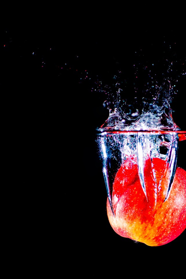 Красное яблоко падает в воду на черном фоне