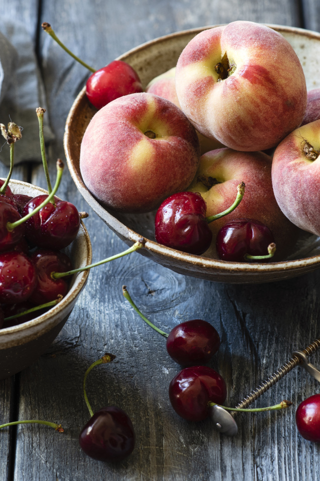 Спелые персики в миске на столе с черешней