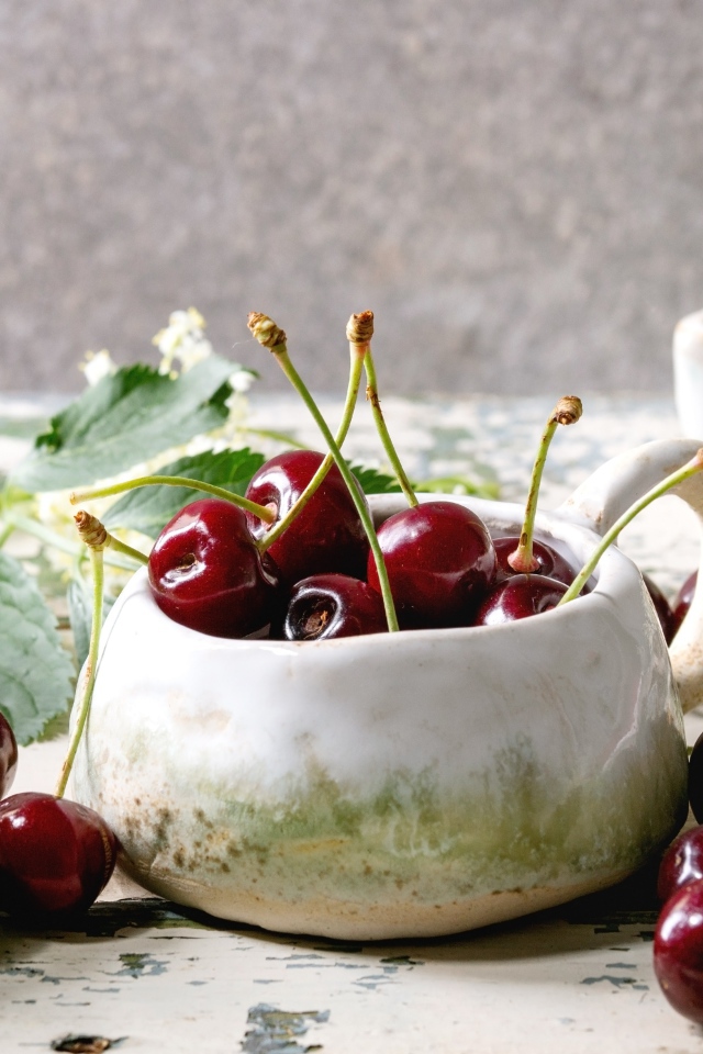 Спелые красные черешни на столе в белом чайнике