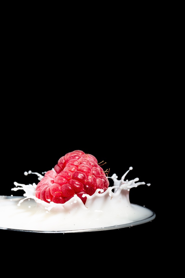 Спелая красная малина с ложке с молоком на черном фоне